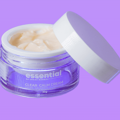 Frasco aberto de creme facial Essential Clear Calm Cream com tampa branca sobre fundo lilás.