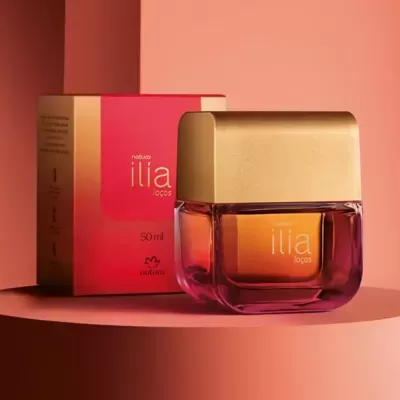 Frasco de perfume Natura Ilía Laços 50 ml com embalagem vermelha e dourada em fundo rosa