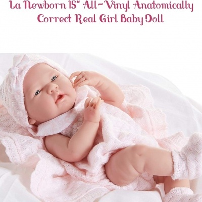 Boneca bebé anatómica vestida com roupas rosa clara deitada sobre tecido branco