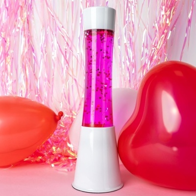 Lâmpada de lava rosa com balões coloridos e cortina metálica rosa ao fundo