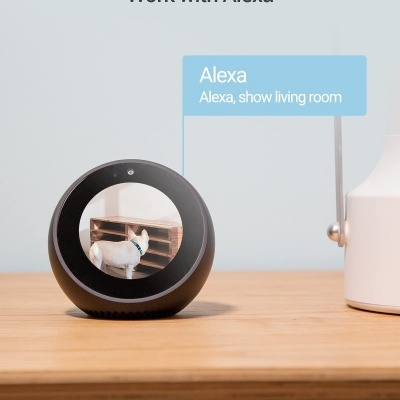 Dispositivo Alexa redondo preto numa mesa de madeira clara com texto de comando Alexa