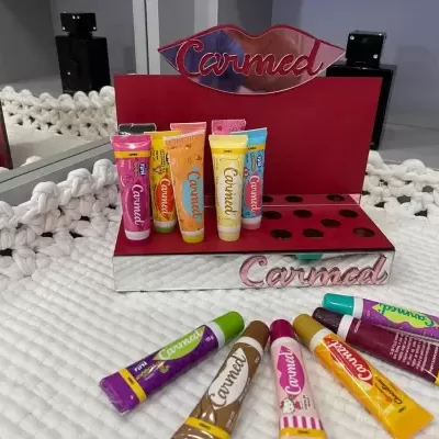 Conjunto de tubos de batom Carmed coloridos em suporte vermelho sobre tecido branco trançado