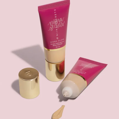 Dois tubos de creme cor de rosa e ouro com texto branco e creme bege saindo de um tubo