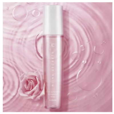 Frasco de perfume rosa sobre superfície rosa com gotas e rosa ao lado