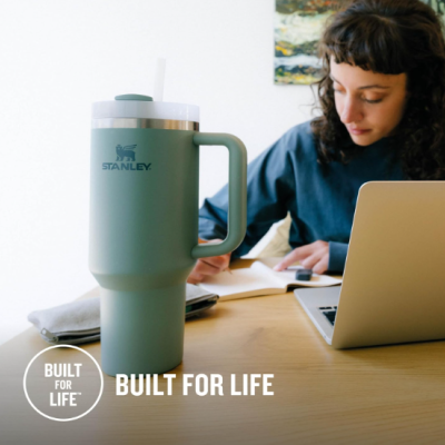 Copo térmico Stanley verde com tampa e canudo branco numa mesa de madeira