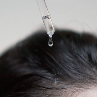 Conta-gotas a pingar líquido sobre cabelo castanho escuro