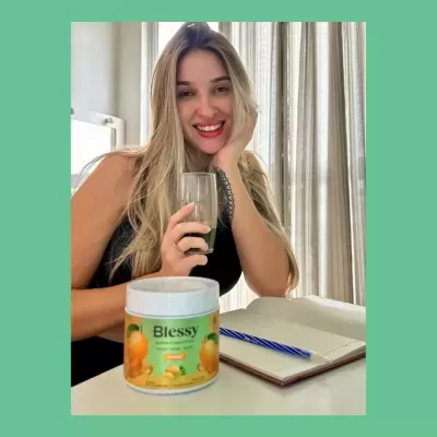Embalagem do suplemento Blessy numa mesa com caderno e caneta, mulher loira ao fundo