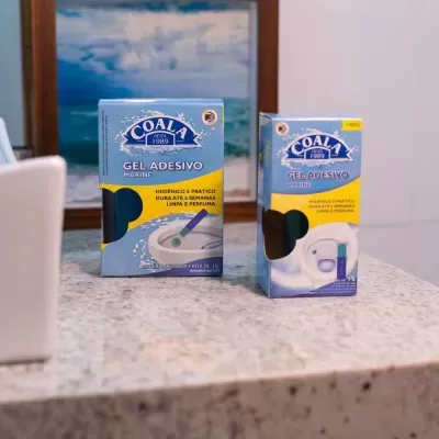 Dois frascos de gel adesivo Coala azul e amarelo sobre uma superfície de pedra cinzenta com pintura de praia ao fundo