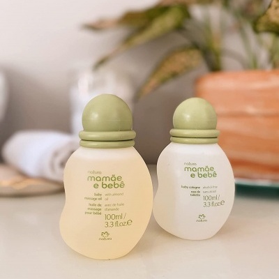 Dois frascos Natura mamãe e bebê, um amarelo e um branco, com tampas verdes, em superfície branca