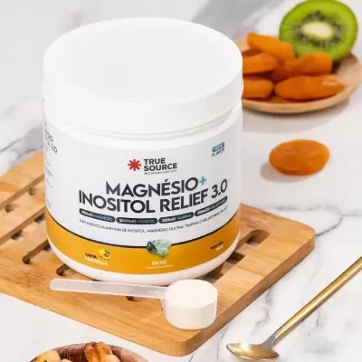 Frasco de suplemento Magnésio+ Inositol Relief 3.0 com colher de pó sobre suporte de madeira.