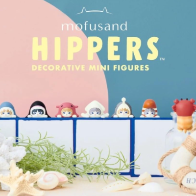 Figuras miniatura decorativas mofusand HIPPERs coloridas atrás de tabuleiro azul e branco com conchas e plantas