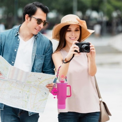 Casal jovem com mapa e câmara, garrafa térmica rosa pendurada no braço da mulher.