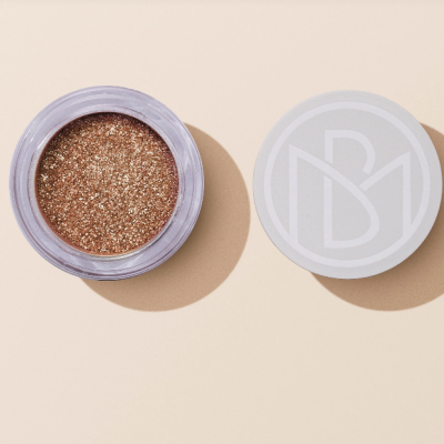 Pote aberto de sombra de olhos dourada com tampa branca ao lado