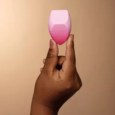 Esponja de maquilhagem rosa em mão com fundo bege