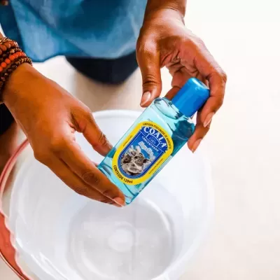 Frasco de limpador perfumado COALA concentrado segurado por mãos sobre balde branco