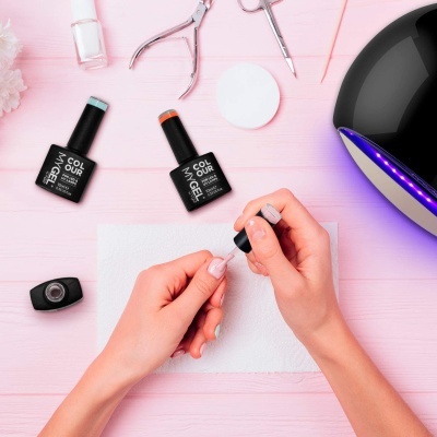 Mãos a aplicar verniz transparente com pincel em unhas com materiais de manicure e lâmpada UV/LED