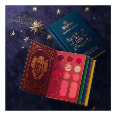 Paleta maquilhagem Harry Potter Gryffindor em livro azul com detalhes dourados e sombras vermelhas e rosas, fundo azul escuro com estrelas douradas