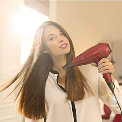 Mulher a usar secador de cabelo vermelho e preto em ambiente interior claro
