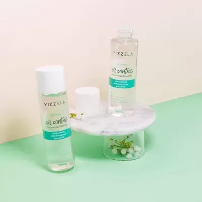 Dois frascos de loção equilibrante VIZZELA oil control em base de mármore e vidro com fundo rosa e verde
