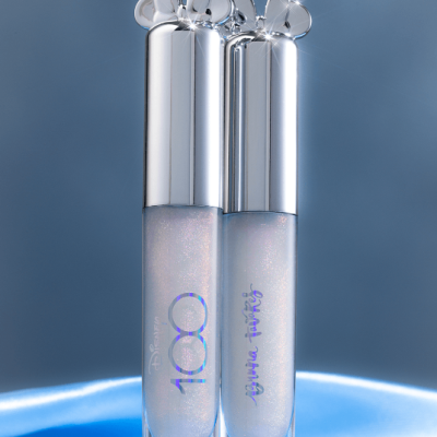 Duas embalagens de gloss de lábios com tampa prateada e detalhes de corações sobre fundo azul.