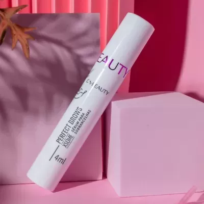 Frasco branco de sérum para sobrancelhas sobre fundo rosa com escovas de sobrancelha e objetos geométricos