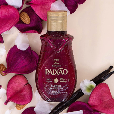 Frasco de óleo corporal Paixão com tampa dourada, rodeado por pétalas de flores e amêndoas