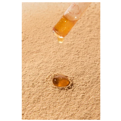 Conta-gotas com líquido âmbar a cair sobre superfície arenosa