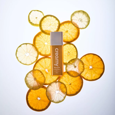 Frasco de creme amarelo com tampa branca e fatias secas de limão e laranja ao redor