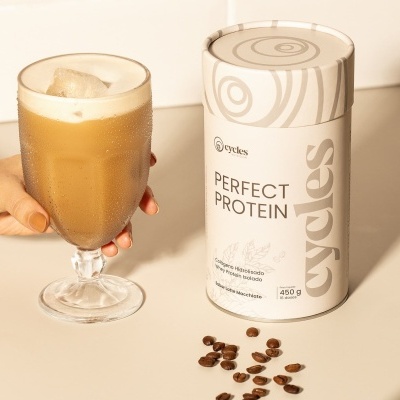 Frasco de proteína em pó cycles Perfect Protein sabor Latte Macchiato com bebida gelada e grãos de café.