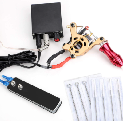 Máquina de tatuagem dourada com punho vermelho, pedal e agulhas embaladas