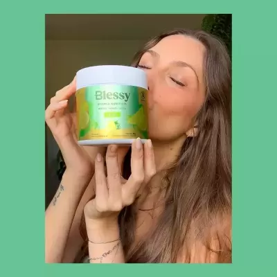 Mulher segurando pote branco com rótulo verde e amarelo de suplemento Blessy limão