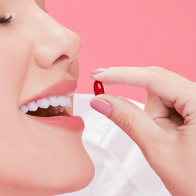 Pessoa a segurar cápsula vermelha perto da boca em fundo rosa