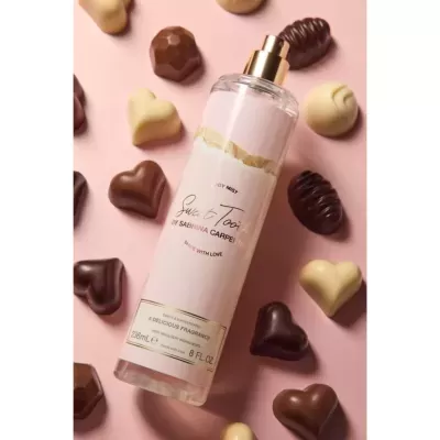 Frasco de spray corporal transparente com bombons em fundo rosa