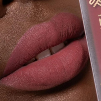 Lábios com batom rosa fosco e pele castanha, embalagem de batom à direita.