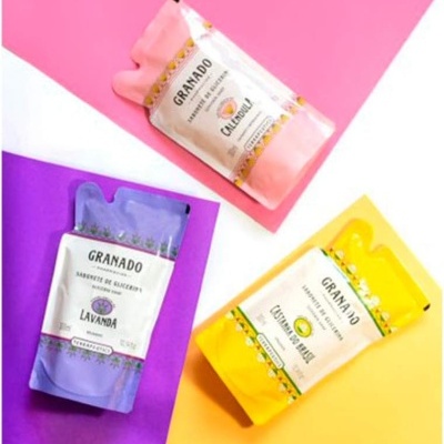 Três embalagens de sabonetes líquidos GRANADO em rosa, roxo e amarelo sobre fundos coloridos correspondentes.