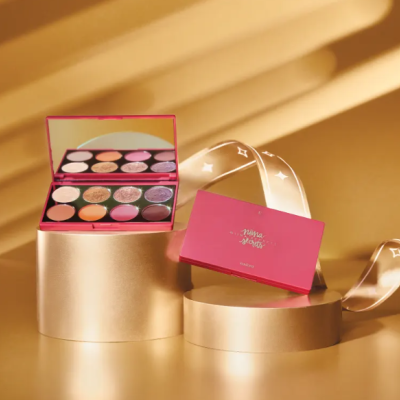 Paleta de sombra de olhos rosa com espelho e várias cores sobre suporte dourado.