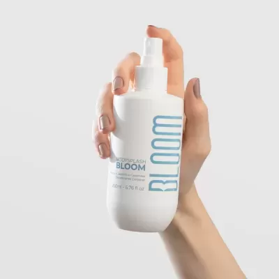 Frasco branco de spray corporal BLOOM com texto azul, na mão de uma pessoa
