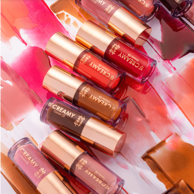 Batons líquidos em várias cores com tampas douradas sobre fundo colorido com amostras de batom.