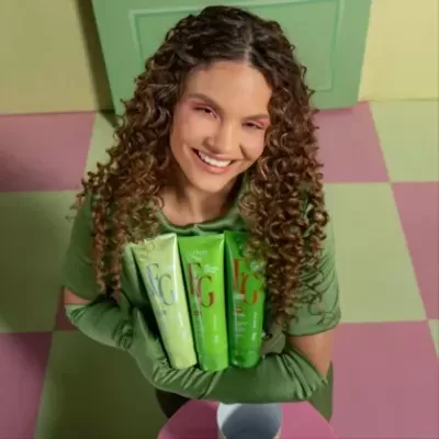 Mulher sorridente segura tubos de creme verde num chão quadriculado rosa e verde