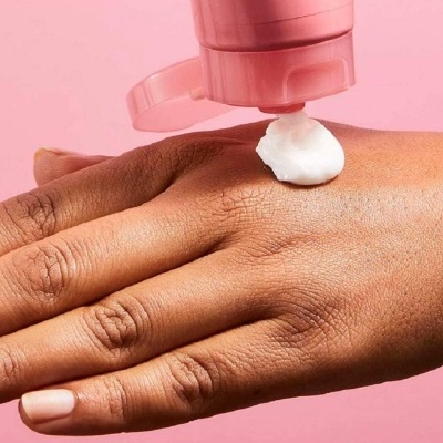 Mão a receber creme branco de tubo rosa sob fundo rosa