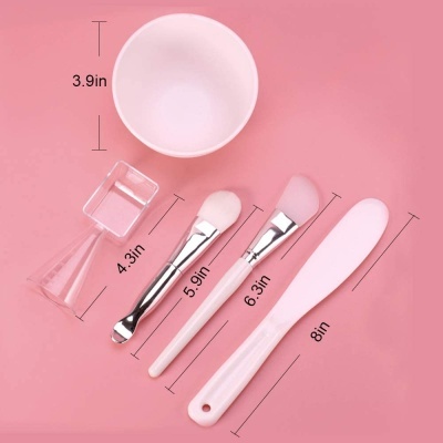 Ferramentas para cuidado facial com tigela, pincéis, espátula e misturador em fundo rosa