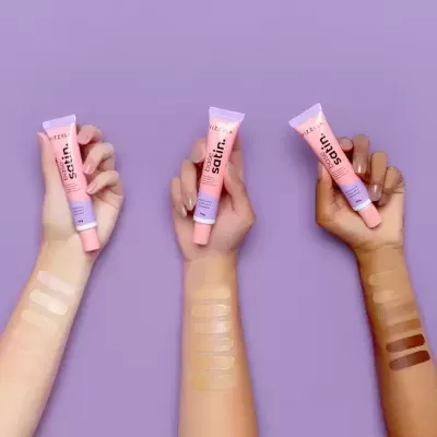 Três braços segurando tubos de creme rosa com amostras no antebraço