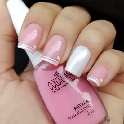 Unhas decoradas com verniz rosa e branco segurando frasco de verniz COLORAMA