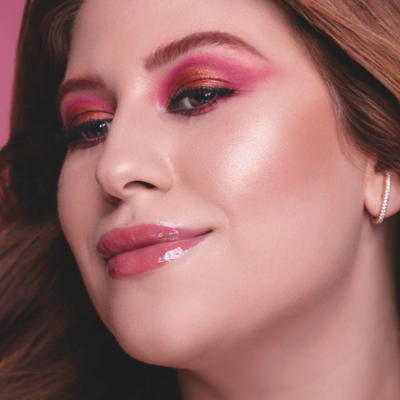 Rosto de mulher com maquilhagem rosa e dourada, cabelo castanho e brincos prateados