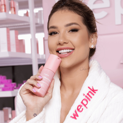 Mulher sorridente com roupão branco segurando produto rosa cosmético