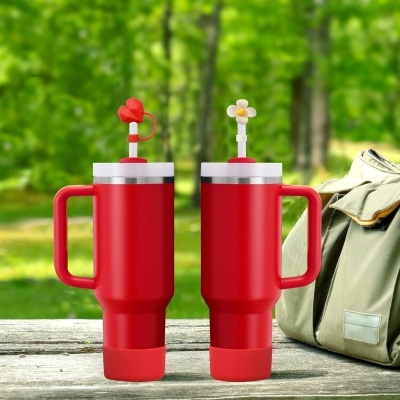 Dois copos térmicos vermelhos com canudos decorados e mochila ao lado sobre mesa em ambiente exterior