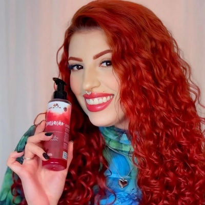 Mulher ruiva encaracolada a segurar frasco de produto vermelho com pump preto