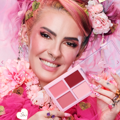 Paleta de maquilhagem com cinco tons em caixa rosa segurada por mulher com cabelo rosa e acessórios florais