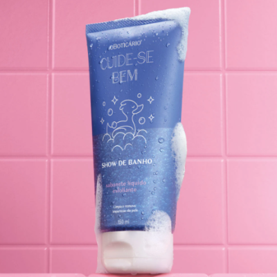 Frasco azul de sabonete líquido esfoliante com espuma sobre azulejos cor-de-rosa