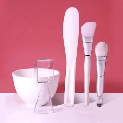 Conjunto de aplicação de máscara facial com pincel, espátula, aplicador, suporte e tigela em fundo rosa